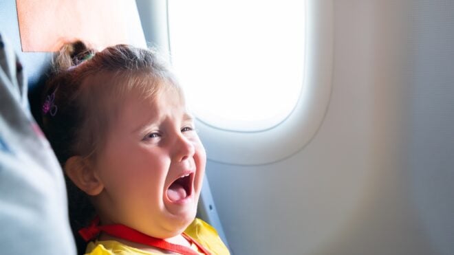A toddler is seen crying while riding an airplane.
