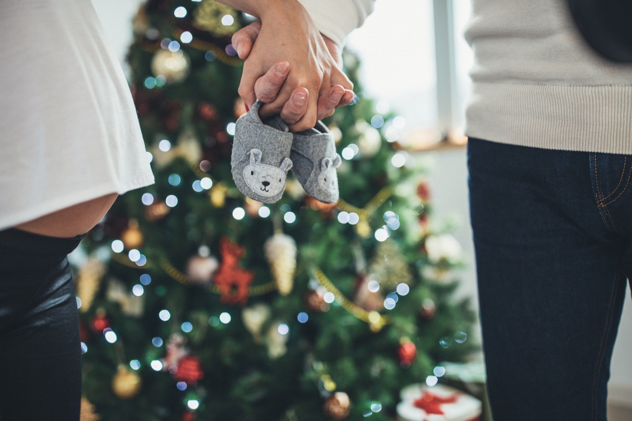 Man and woman, married couple relaxing together at home, standing next to Christmas day. holding baby shoes.