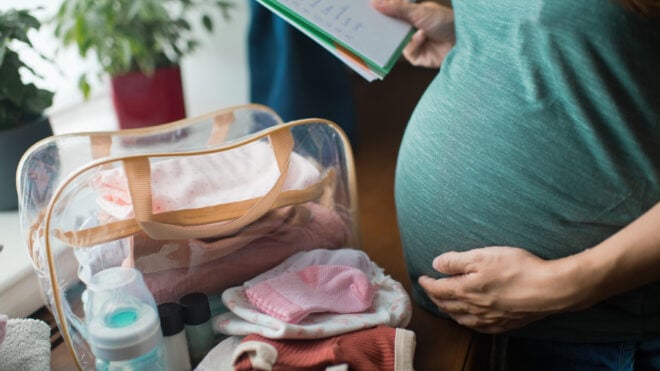 Pregnant woman at home preparing bag for newborn baby