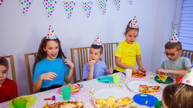The group of little friends eating at the birthday party. The kids are eating pizza and talking