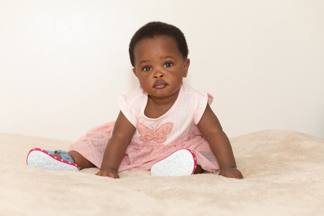 Portrait of a black baby girl dressed in pink sitting on a bed