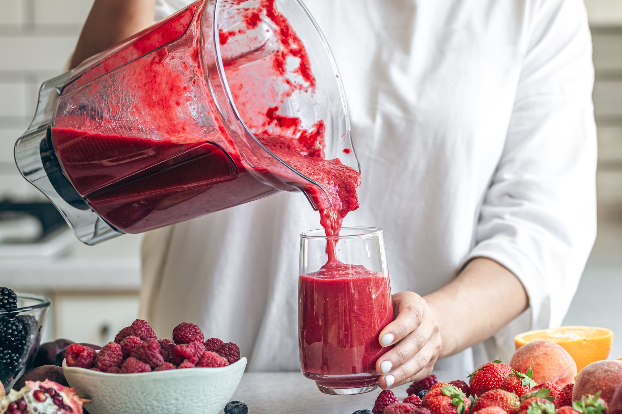 A woman making detox smoothie at home, woman pouring red smoothie to glass, healthy food concept.