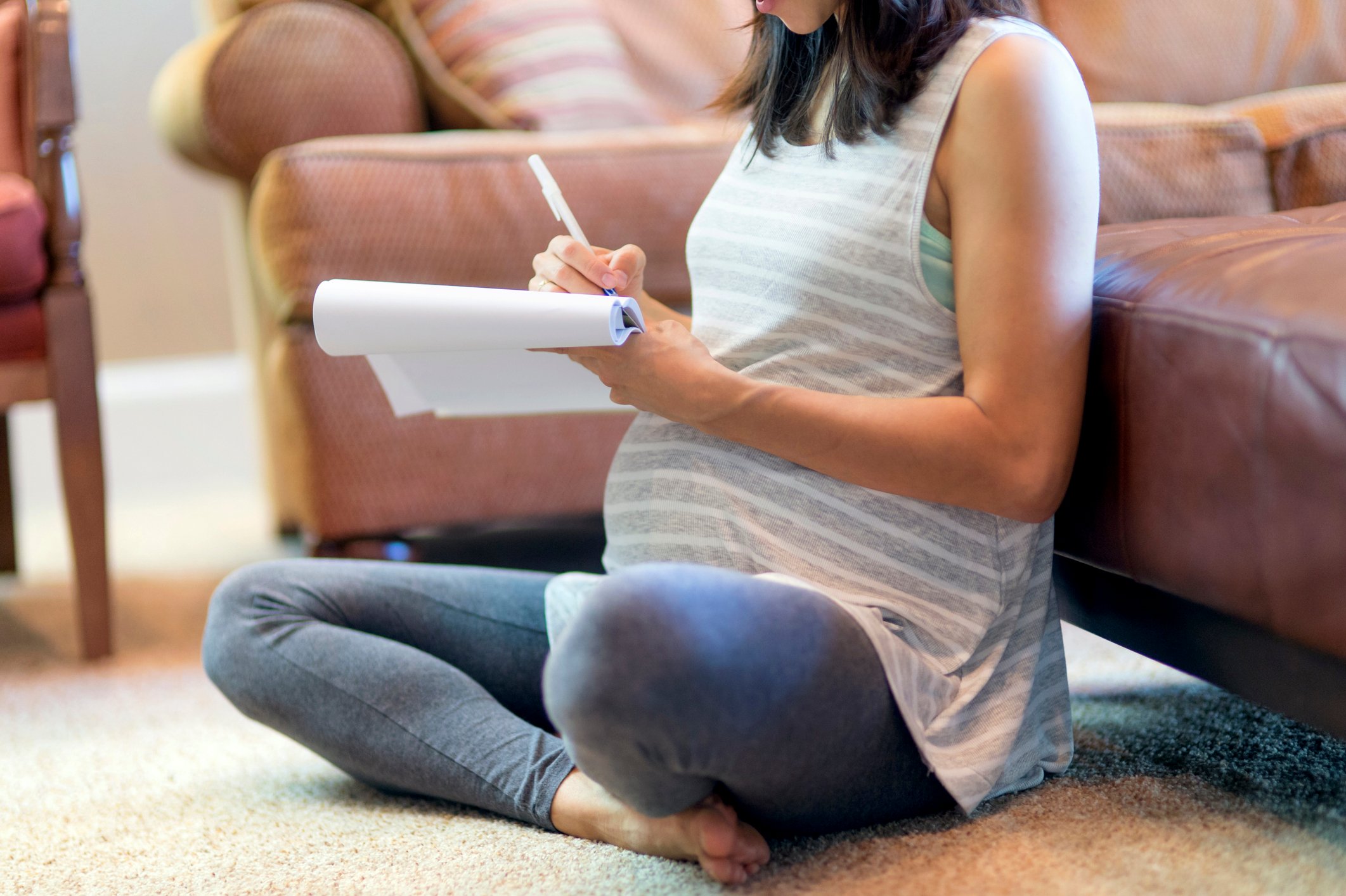 Pregnant mother sitting on carpet using a pad and paper